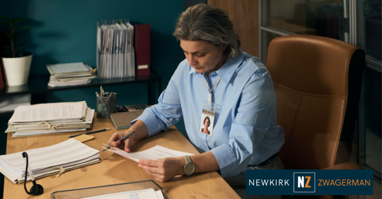 Middle aged Caucasian woman sitting at desk reviewing paperwork in office environment,
